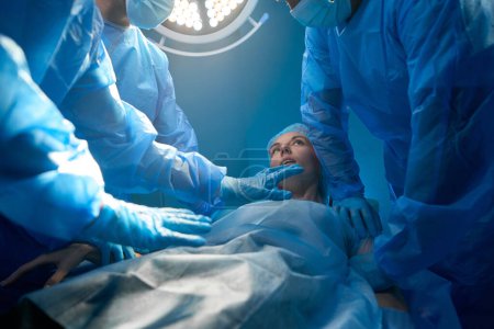 Foto de Paciente mujer despertando después de la cirugía rodeada de un equipo médico profesional en quirófano - Imagen libre de derechos