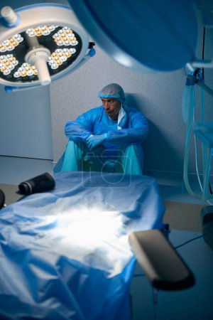 Photo for Tensed surgeon man sitting on floor in operating room in hospital - Royalty Free Image