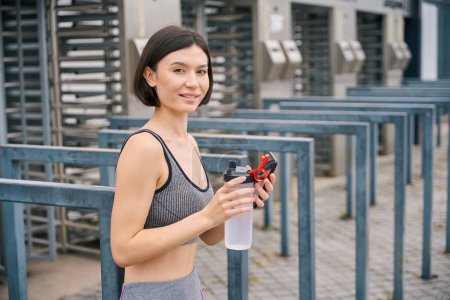 Téléchargez les photos : Jeune femme en vêtements sportifs tenant une bouteille d'eau et se préparant à l'entraînement du matin. Concept de sport - en image libre de droit