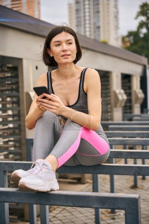 Téléchargez les photos : Jeune femme en vêtements sportifs tenant smartphone et bavardage. Concept de sport en dehors - en image libre de droit