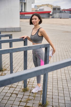 Foto de Mujer fuerte en ropa deportiva estira los músculos de las piernas. Concepto de estilo de vida saludable. Entrenamiento al aire libre - Imagen libre de derechos
