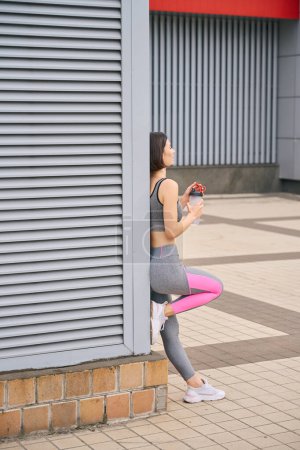 Photo for Sporty lady tired after hard training, standing outside, holding bottle of water. Morning sport - Royalty Free Image