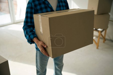 Cropped picture of cardboard box held in male hands while man standing in room during house removal