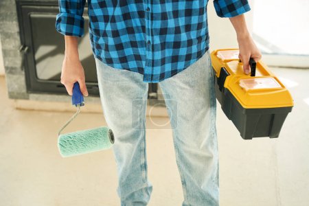 Foto de Manos del hombre que sostiene el rodillo de pintura en una mano y y caja de herramientas en otra - Imagen libre de derechos