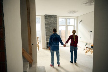 Foto de Imagen de vista trasera de la señora y el hombre de pie en una habitación incompleta mientras se sostienen mutuamente a mano - Imagen libre de derechos