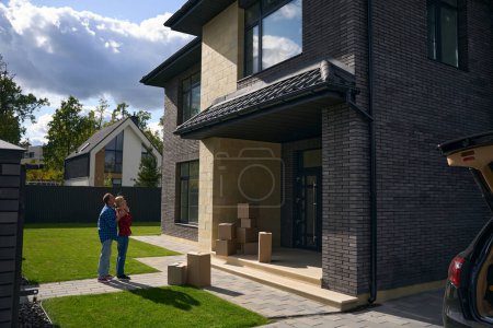 Photo for Full length photo of man standing behind woman in front yard and looking at new house - Royalty Free Image