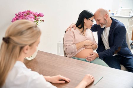 Foto de Hombre adulto y su esposa embarazada felices que tienen un bebé sano en el útero, controlando el embarazo en una clínica privada de ginecología y reproductología - Imagen libre de derechos