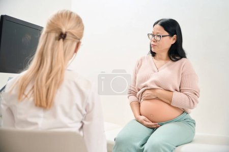 Schwangere erwachsene Frau klagt über Beschwerden im Bauch, spürt keine Bewegung im Bauch, Ultraschallspezialist überprüft Zustand des Babys im Mutterleib