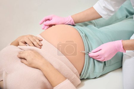Foto de Ginecólogo de cerca que realiza la inyección de inmunoglobulina Rh en el vientre de la mujer embarazada, procedimiento necesario debido al riesgo de incompatibilidad Rh - Imagen libre de derechos
