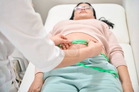 Photo for Qualified gynecologist checking the volume of belly of pregnant lady who came at routine health check-up in third trimester, woman preparing for baby delivering - Royalty Free Image