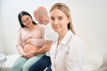 Médico ginecólogo altamente calificado reproductólogo mirando a la cámara y sonriendo, feliz de ayudar a las personas que luchan para conseguir un bebé, clínica de fertilización invitro, publicidad