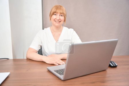 Femme thérapeute souriante tenant rendez-vous médical des citoyens dans son bureau confortable, dactylographiant les dossiers médicaux sur ordinateur portable, les soins de santé et la médecine