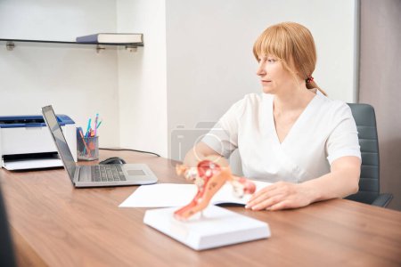 Photo for Female practitioner in light uniform sitting in her office with laptop and conducting appointment online, consulting woman about her reproductive health - Royalty Free Image