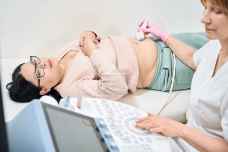 Foto de Sonógrafa mujer concentrada realizando ultrasonido de órganos abdominales de paciente asiático adulto, chequeo rutinario de salud en clínica privada, salud y medicina - Imagen libre de derechos