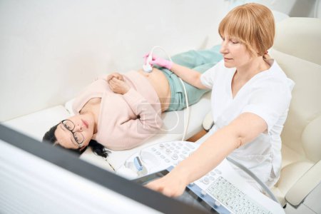 Photo for Female ultrasound specialist performing procedure and pointing at digital display with image, showing health problems to asian female patient, health check-up - Royalty Free Image