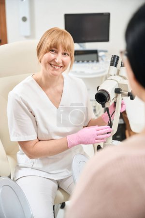 Foto de Ginecóloga sonriente que muestra el microscopio que usa para un mejor examen pélvico y para verificar cualquier cambio inusual, chequeo de salud de rutina femenina - Imagen libre de derechos