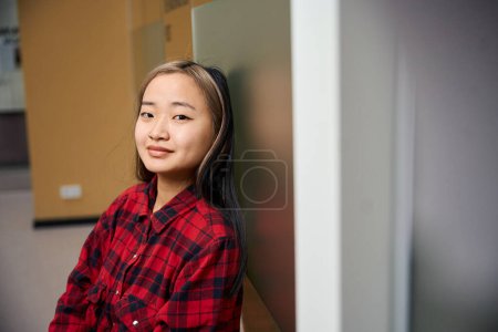 Foto de Recortado joven seria asiático femenino IT empleado mirando cámara por pared en coworking oficina. Concepto de trabajo independiente o remoto moderno - Imagen libre de derechos
