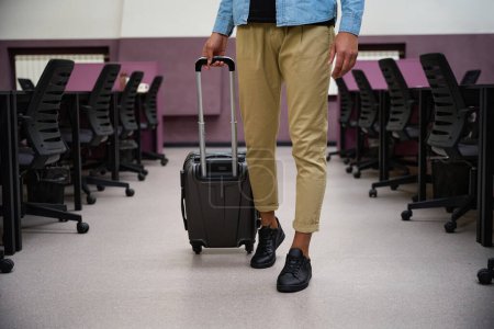 Photo for Close up picture of legs of man who walking in call center and wheeling trolley bag in hand - Royalty Free Image