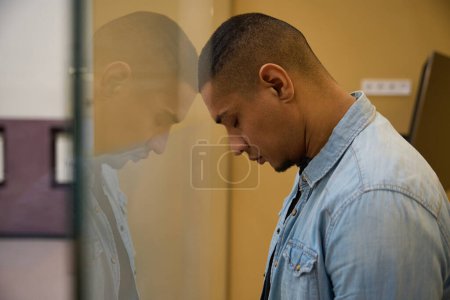 Téléchargez les photos : Vue de côté photo de frustré afro-américain gars fermé les yeux et appuyé sa tête sur une cloison en verre - en image libre de droit
