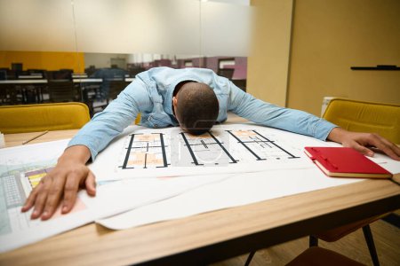 Téléchargez les photos : Employé afro-américain surmené assis à table dans l'espace de travail tout en étant couché dessus et en dormant - en image libre de droit