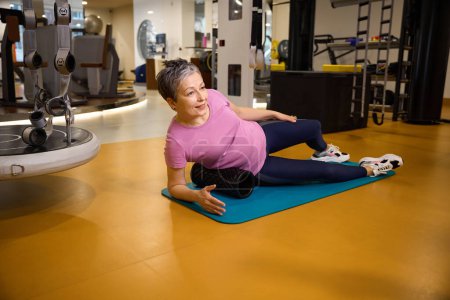 Photo for Middle aged caucasian woman wearing sportswear doing sport exercise on fitness mat in gym. Concept of modern healthy lifestyle - Royalty Free Image