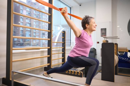 Photo for Smiling middle aged caucasian woman wearing sportswear stretching with rope in rehabilitation gym. Concept of modern healthy lifestyle - Royalty Free Image
