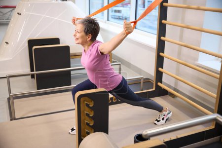 Photo for Smiling middle aged caucasian woman wearing sportswear stretching with rope after injury in rehabilitation gym. Concept of modern healthy lifestyle - Royalty Free Image