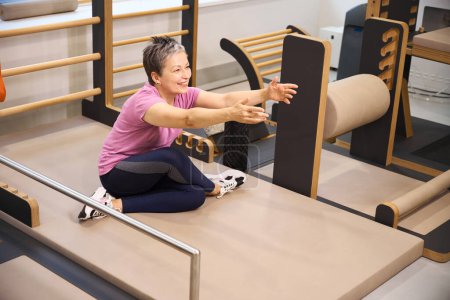 Photo for Smiling adult caucasian woman wearing sportswear stretching after injury during recovery in rehabilitation gym. Concept of modern healthy lifestyle - Royalty Free Image