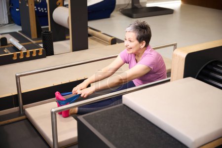 Photo for Smiling mature caucasian woman wearing sportswear stretching with resistance band in rehabilitation gym. Concept of modern healthy lifestyle - Royalty Free Image