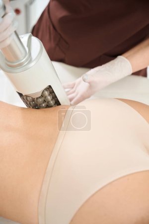 Aesthetic medicine worker using endosphere apparatus for thinning the silhouette, modeling the contours of female client body who need to quickly get in shape