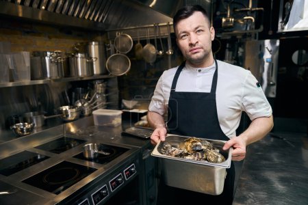Téléchargez les photos : Chef masculin caucasien tenant bol avec huîtres sur la cuisine dans le restaurant. Concept de saine alimentation savoureuse - en image libre de droit