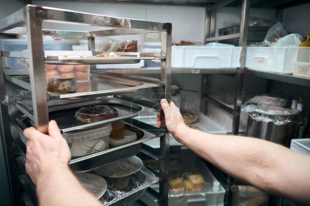Photo for Cropped male chef holding dishes on shelves in refrigerator storage in restaurant. Concept of delicious healthy eating - Royalty Free Image
