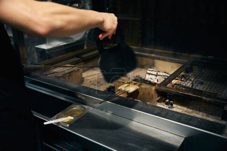 Partial male chef waving over fish fillet frying in burning fire place in restaurant. Concept of delicious healthy eating