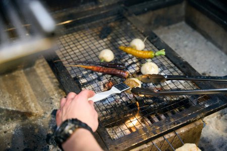 Partial male chef smearing onion with brush and frying vegetables on iron net in burning fire place in restaurant. Concept of tasty healthy eating
