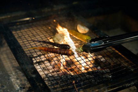 Téléchargez les photos : Légumes d'oignons et de carottes frire sur le filet de fer dans la cheminée brûlante dans le restaurant. Concept de saine alimentation savoureuse - en image libre de droit