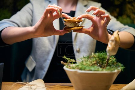 Téléchargez les photos : Femme partielle tenant marshmallow friture dans les biscuits à la table en bois dans le restaurant. Concept de délicieuse alimentation saine - en image libre de droit