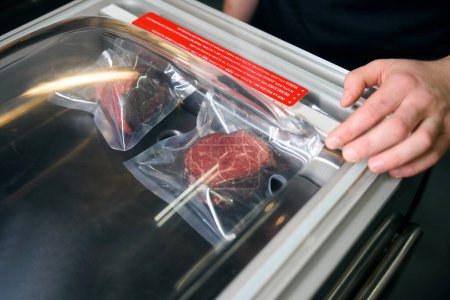 Téléchargez les photos : Homme chef masculin partiel mettant la viande sous vide au réfrigérateur pour le stockage dans le restaurant. Concept de délicieuse alimentation saine - en image libre de droit