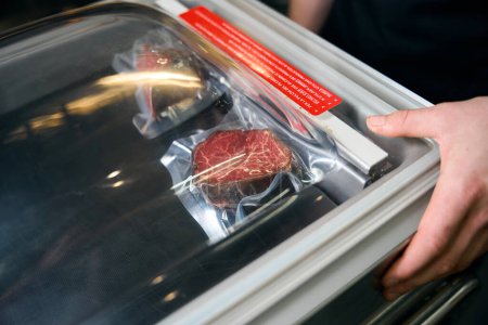 Téléchargez les photos : Cultivé homme chef mettant la viande sous vide au réfrigérateur pour le stockage dans le restaurant. Concept de saine alimentation savoureuse - en image libre de droit