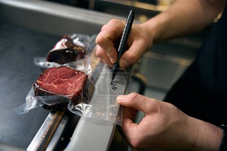 Photo for Partial male chef man drawing date with marker on vacuum meat in refrigerator for storage in restaurant. Concept of tasty healthy eating - Royalty Free Image