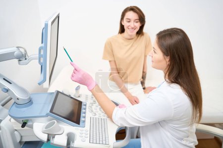 Photo for Focused female caucasian gynecologist showing to young smiling european woman her results of pregnant belly ultrasound scanning in clinic. Concept of pregnancy and maternity - Royalty Free Image