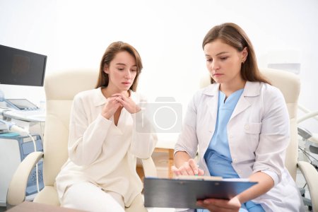 Photo for Female caucasian doctor showing to young tense european woman her examining results in clinic. Concept of health care - Royalty Free Image