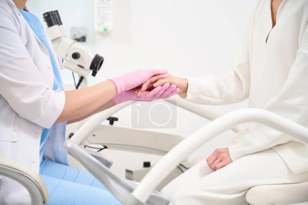 Foto de Vista lateral recortada de una ginecóloga y una paciente tomadas de la mano en la clínica. Concepto de asistencia sanitaria - Imagen libre de derechos