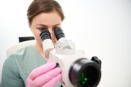 Téléchargez les photos : Vue recadrée du médecin caucasien concentré féminin portant l'uniforme médical regardant au microscope pendant le travail en clinique. Concept de soins de santé - en image libre de droit