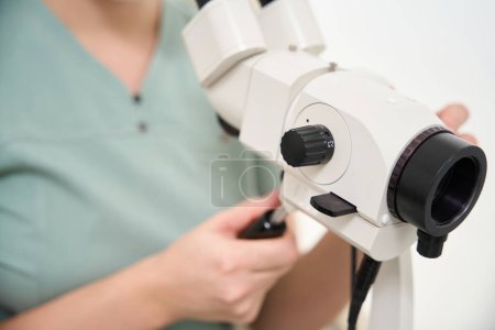 Téléchargez les photos : Concentration sélective du microscope dans les mains d'une femme médecin partiellement floue pendant le travail en clinique. Concept de soins de santé - en image libre de droit