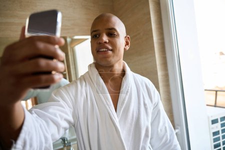 Téléchargez les photos : Jeune homme afro-américain utilisant un téléphone portable dans la salle de bain le matin. Concept de style de vie moderne - en image libre de droit