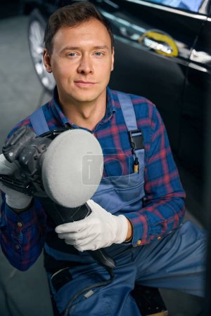 Foto de Retrato de hombre en uniforme instrumento de sujeción para pulir el detalle del coche. Preparación de la superficie antes de pintar - Imagen libre de derechos