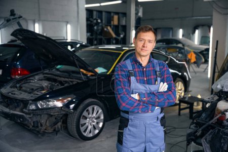 Photo for Portrait of smiling worker standing in workspace near car with open hood. Car repair concept - Royalty Free Image
