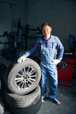 Téléchargez les photos : Employeur en uniforme de protection et gants debout près de la roue, travaillant et effectuant des réparations dans le montage des pneus - en image libre de droit