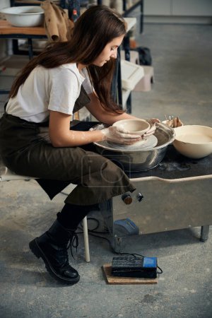 Photo for Female potter engaged in craft in workshop on potters wheel and making clay product - Royalty Free Image