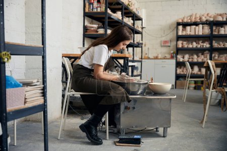 Téléchargez les photos : Femme concentrée faisant pot en utilisant la roue de poterie en studio créatif - en image libre de droit